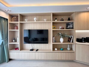 A modern living room with a large flat-screen TV, wooden shelving, and various decorative items. - New 2 Bedrooms with Terrace by Viva Riviera (Cannes)
