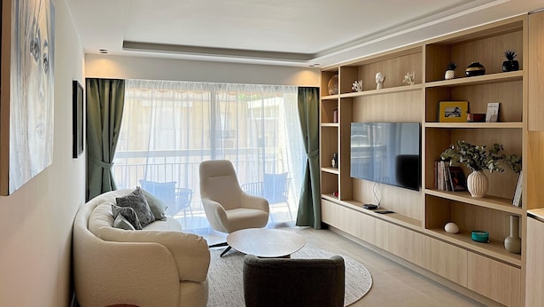 Ein modernes Wohnzimmer mit Sofa, Sesseln, Couchtisch und Fernseher auf einer Holzablage.