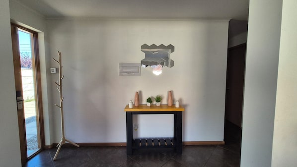 A hallway with a dark floor, a coat rack, a wall-mounted light fixture, and a small console table with decorative items.