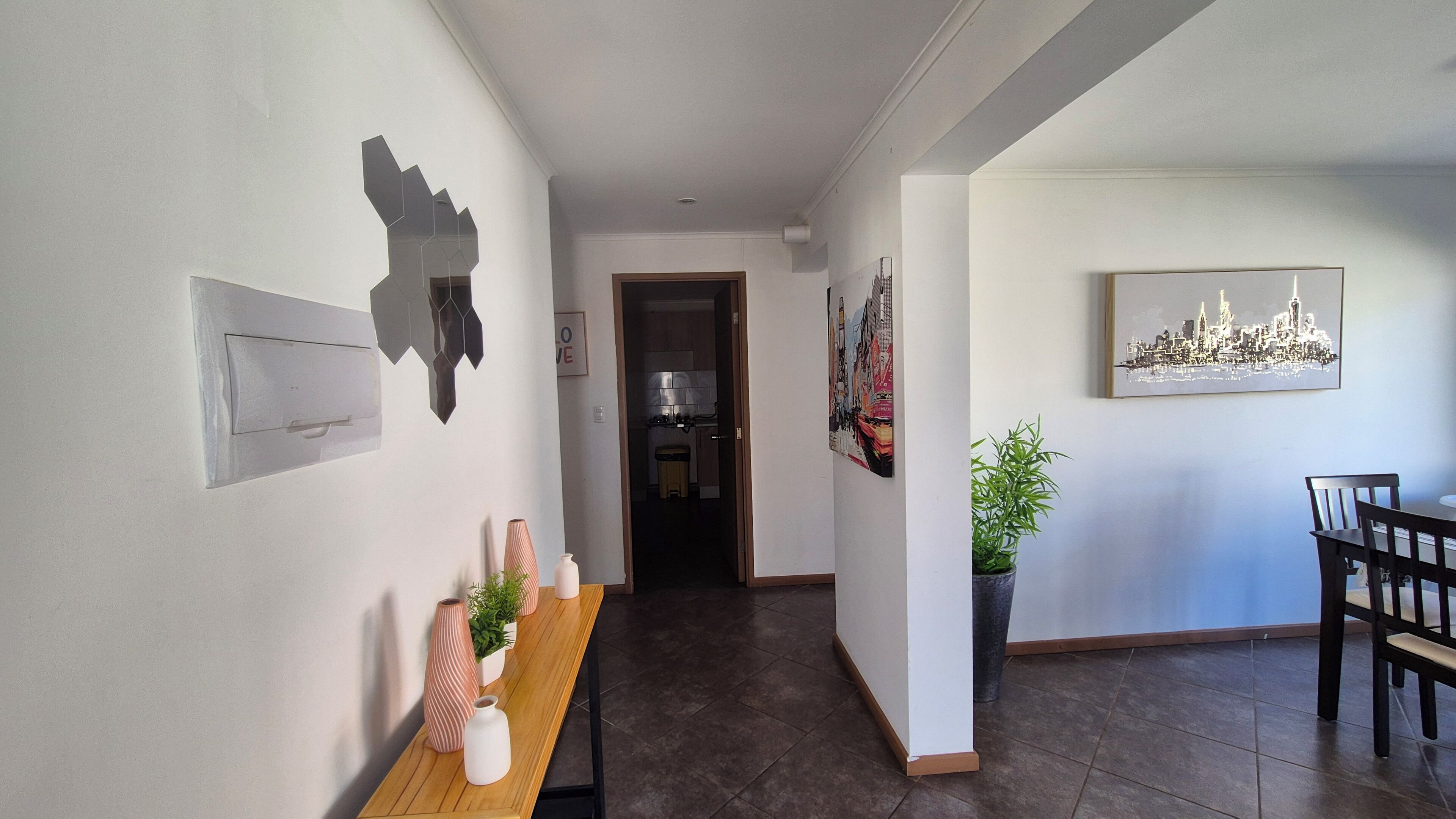 Un pasillo con un banco de madera, una planta en maceta y una zona de comedor con una silla y una mesa.