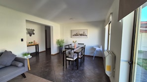 A dining area with a table and chairs, a sofa, a potted plant, and a cityscape painting on the wall.