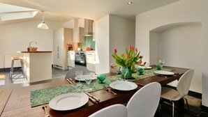 Un comedor moderno con una mesa de madera dispuesta para cuatro, una cocina al fondo y vistas al área de estar.