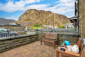 A patio with a stone wall, a wooden bench, and a table with a tray of teapots and cups. - Charming Snowdonia Slate Cottage (Blaenau Ffestiniog)