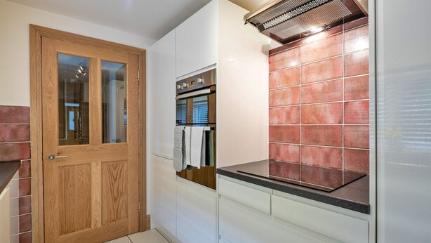 Eine Küche mit Holztür, eingebautem Backofen und einer gefliesten Spritzschutzwand.
