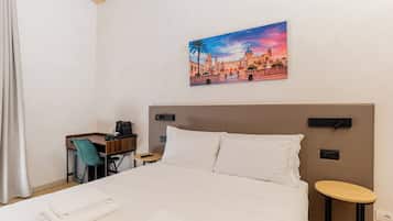 Een hotelkamer met een bed, een bureau, een stoel, een tafeltje en een schilderij aan de muur.