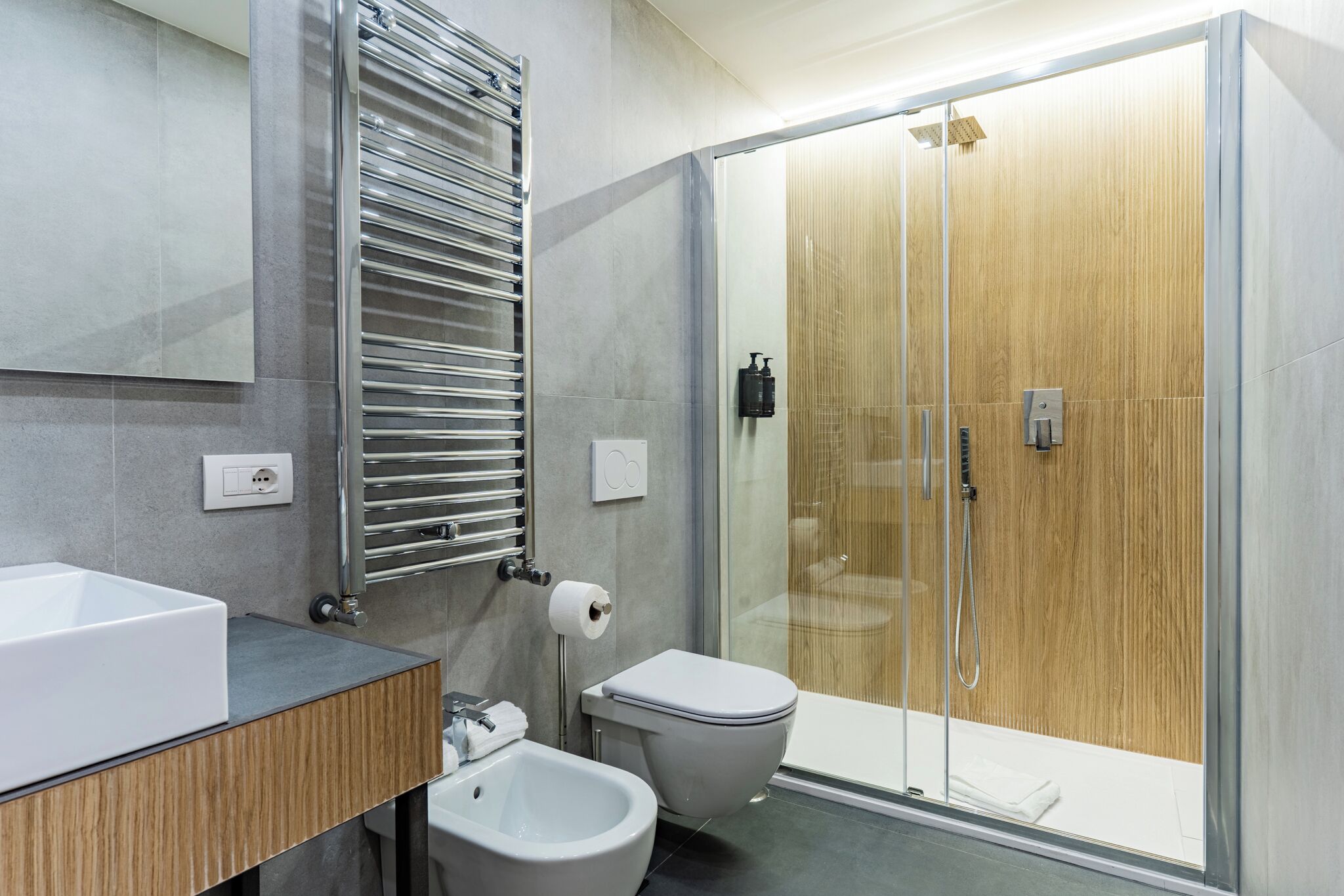 A modern bathroom with a glass-enclosed shower, a white sink, and a bidet.