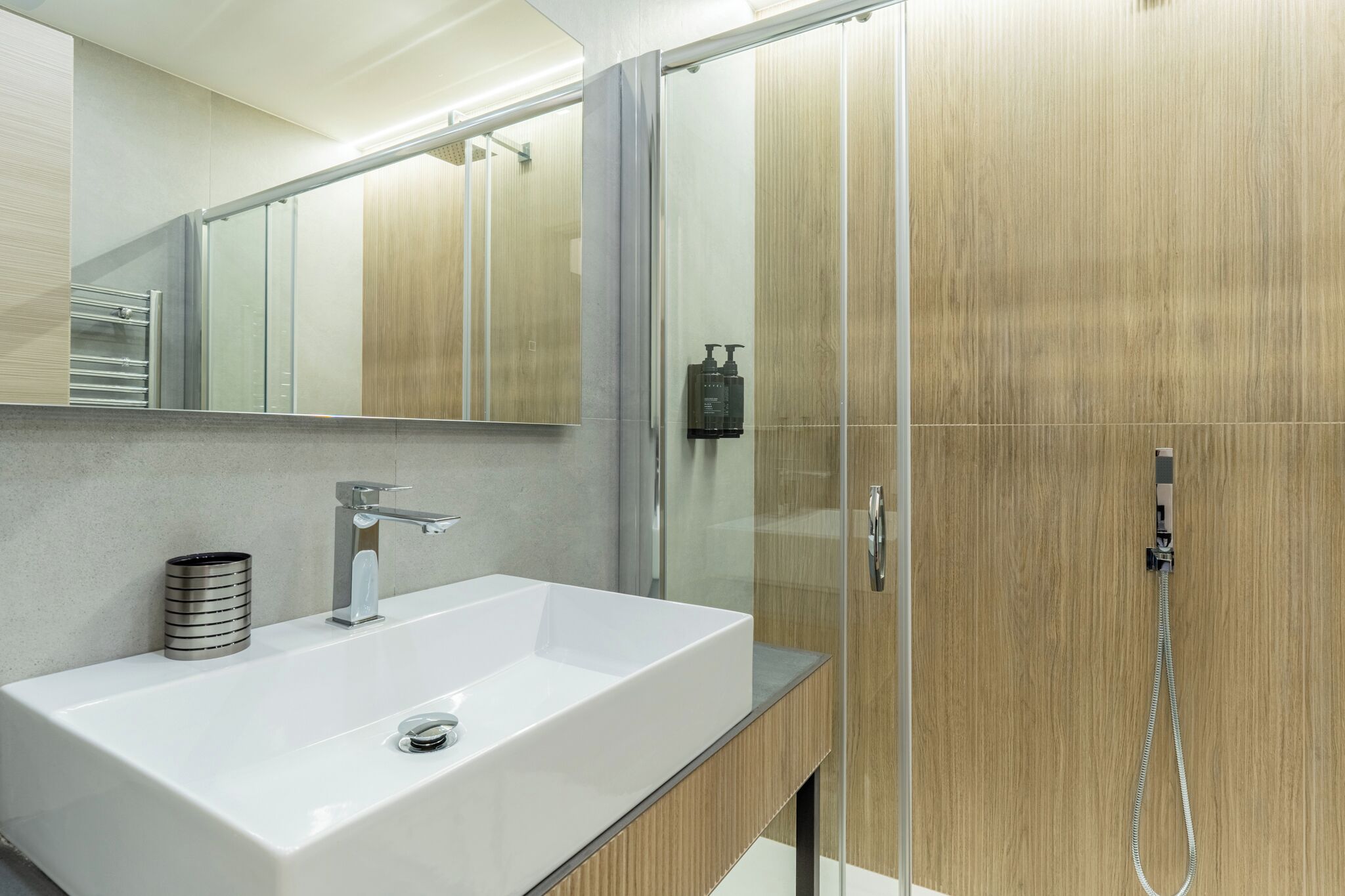 A modern bathroom with a large white sink, a mirror, and a glass shower enclosure.