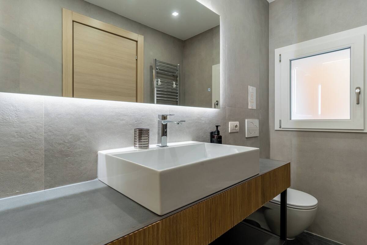 Un baño moderno con un lavamanos grande de color blanco, tocador de madera y un inodoro.