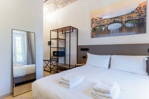 A hotel room with a bed, a mirror, a wardrobe, a desk, and a painting of a cityscape.