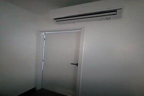 A closed door with a handle, a white wall, and an air conditioning unit mounted above it. - Studio privativo em BG a 2km da praia (Cajueiro da Praia)