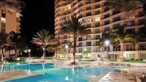 A swimming pool area with a large pool, palm trees, and a multi-story hotel building in the background. - Dream Stay (Fort Myers)