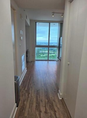 A hallway with wooden flooring leading to a large window with a view of greenery. - Dream Stay (Fort Myers)