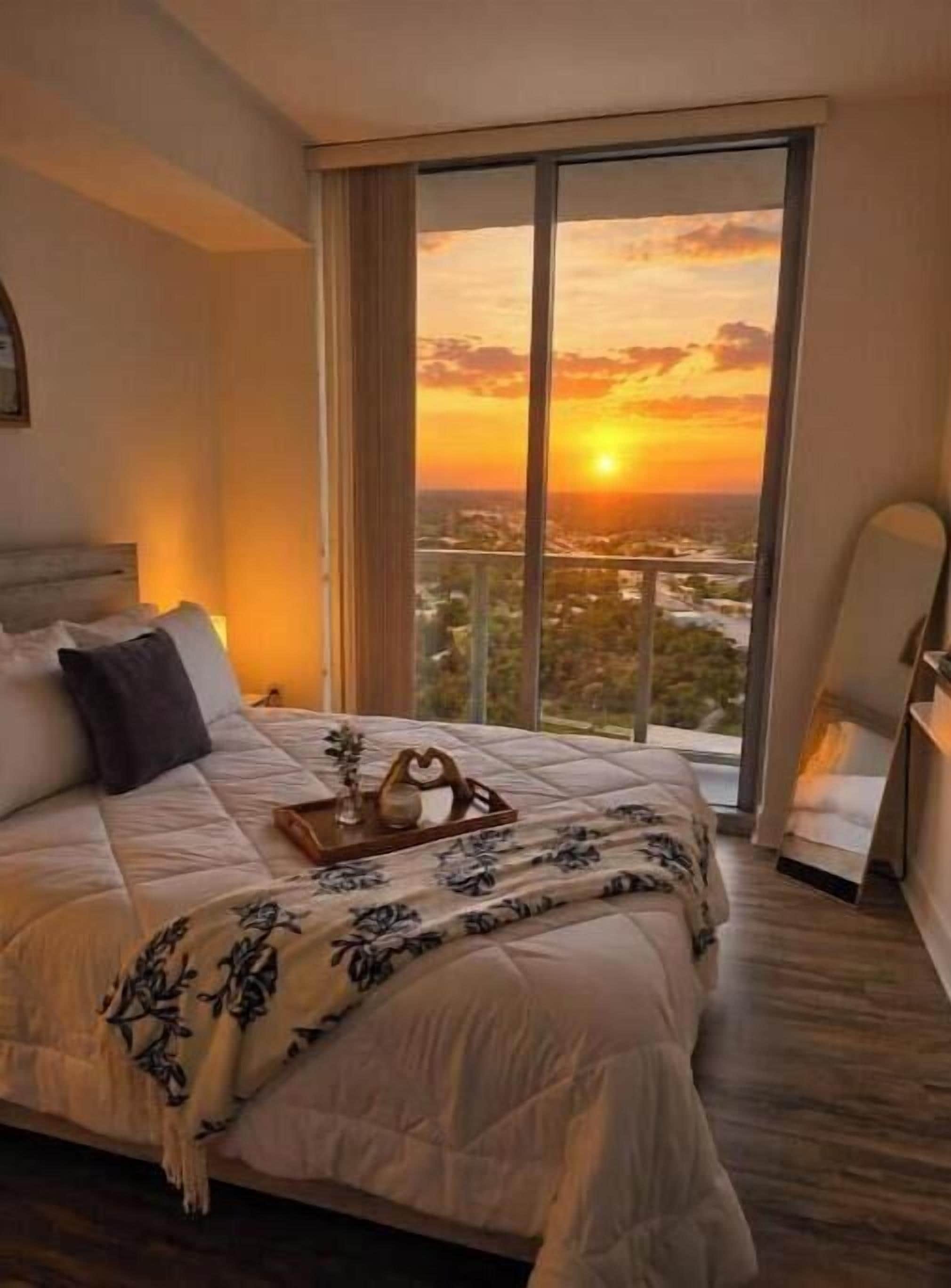Une chambre d’hôtel avec un grand lit, une vue sur le coucher de soleil et un panorama sur la ville.