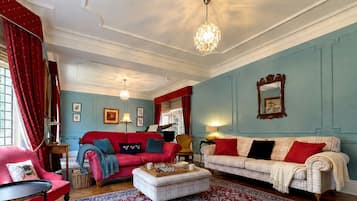 Una habitación con un sofá rojo, un sofá blanco, un sillón rojo y una alfombra estampada.