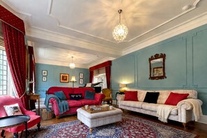 A room with a red sofa, a white sofa, a red armchair, and a patterned rug.