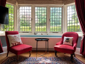 Una habitación con dos sillones rojos, una mesita y un ventanal con vistas a zonas verdes.