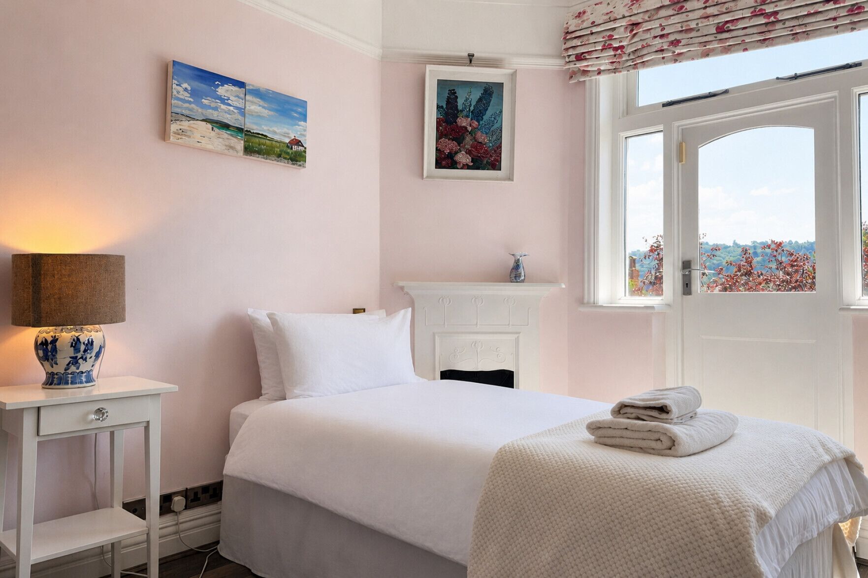 A bedroom with a bed, a bedside table with a lamp, a dresser, and a window with a view.