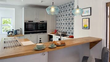 Eine moderne Küche mit Holzarbeitsplatte, zwei hängenden Pendelleuchten, einer Kaffeemaschine und einer Frühstücksvorrichtung mit Croissants und einer Tasse Kaffee.