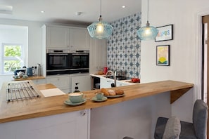 Une cuisine moderne avec un plan de travail en bois, deux lampes suspendues, une machine à café et un coin petit-déjeuner avec des croissants et une tasse de café.