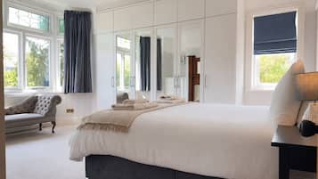 A bedroom with a large bed, a wardrobe, a sitting area with a chair, and a window with curtains.