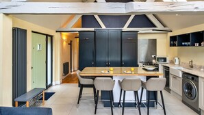 A modern kitchen with a central island, bar stools, a built-in oven, and a washing machine. - Peaceful Dorset Cottage for 4 (Wimborne)