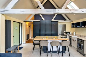 A modern kitchen with a central island, bar stools, a built-in oven, and a washing machine. - Peaceful Dorset Cottage for 4 (Wimborne)