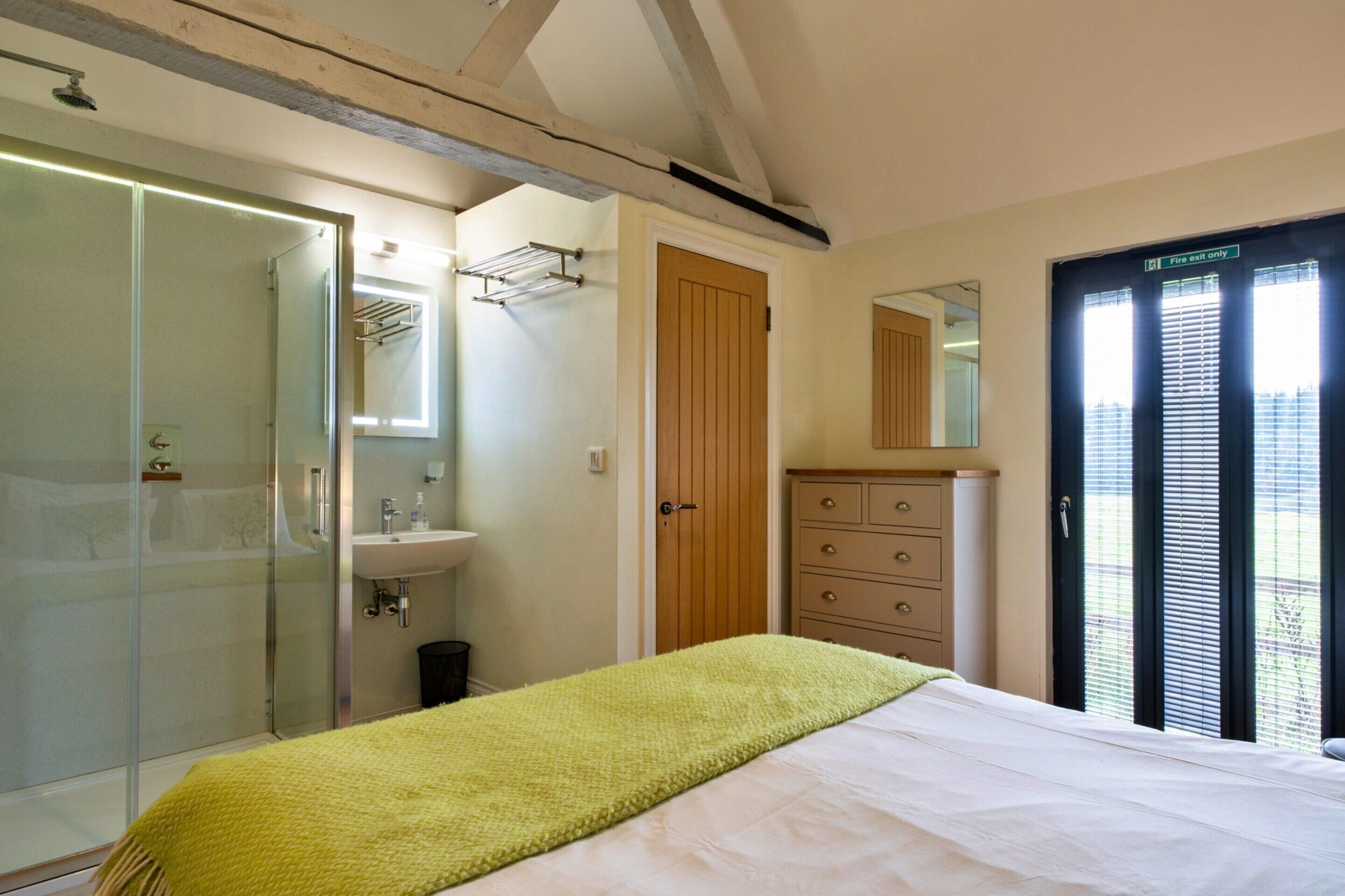 A bedroom with a bed, a bedside table, a mirror, a wardrobe, a bathroom with a shower, and a toilet.