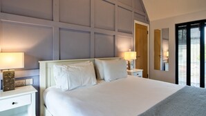 A neatly made bed with white linens, two bedside tables with lamps, a wooden door, and a large mirror on the wall. - Peaceful Dorset Cottage for 4 (Wimborne)