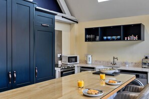 A modern kitchen with dark cabinets, a marble countertop, a built-in microwave, a kettle, and a sink. - Peaceful Dorset Cottage for 4 (Wimborne)