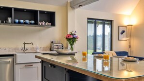 A modern kitchen with a central island, a built-in oven, and a dining area with a sofa and table. - Peaceful Dorset Cottage for 4 (Wimborne)