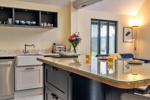 A modern kitchen with a central island, a built-in oven, and a dining area with a sofa and table. - Peaceful Dorset Cottage for 4 (Wimborne)