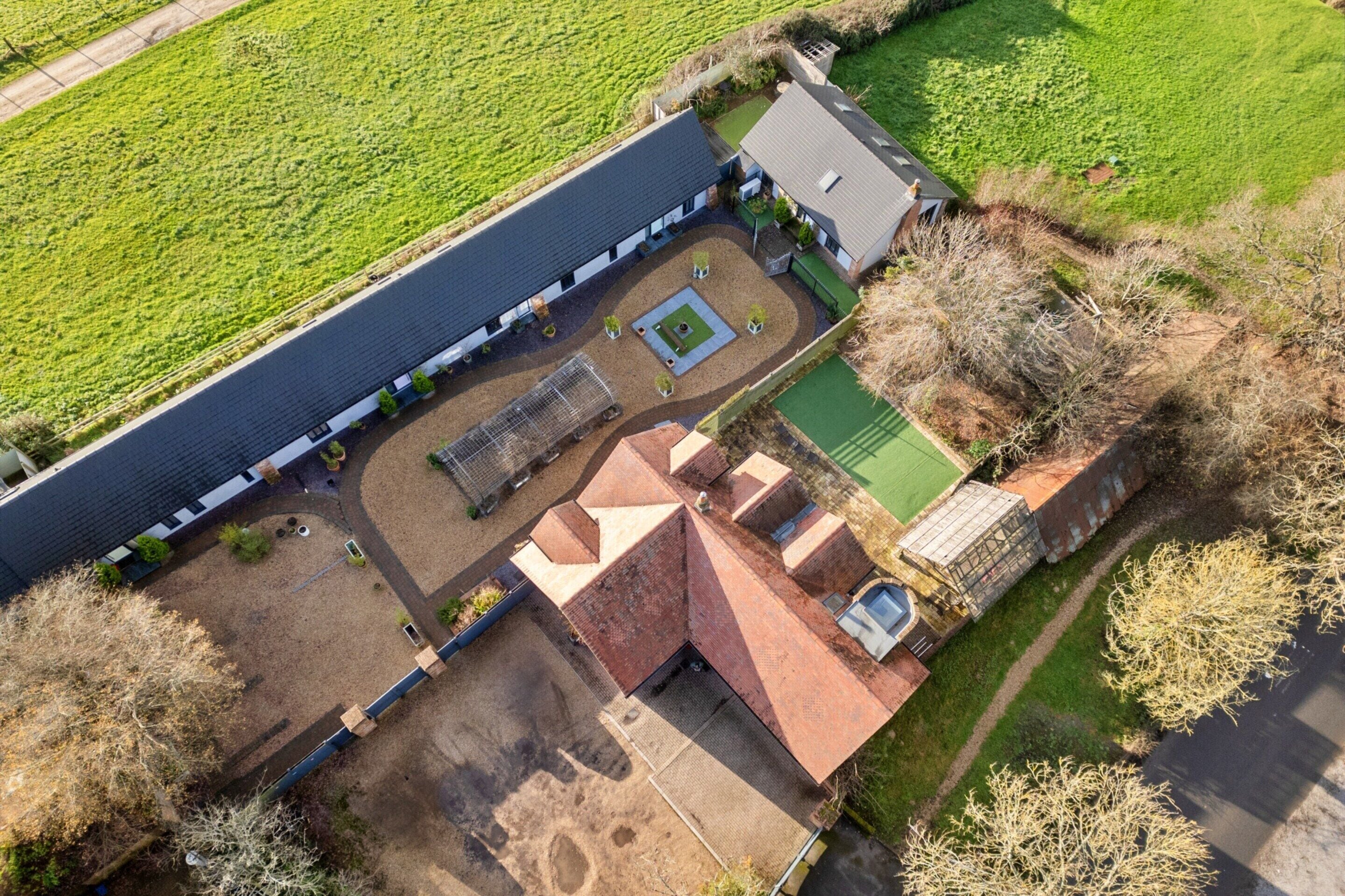 Vista aérea de una propiedad con un edificio alargado, un patio con césped verde y campos circundantes.