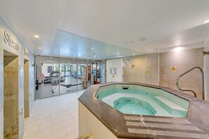 A modern indoor swimming pool with a glass wall, a sauna area, and exercise equipment visible through the glass. - Smart Stay With Fitness Center (London)