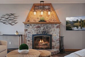 Een open haard van steen met een modern design, een plafondlamp en een lijstwerk met een landschap.'