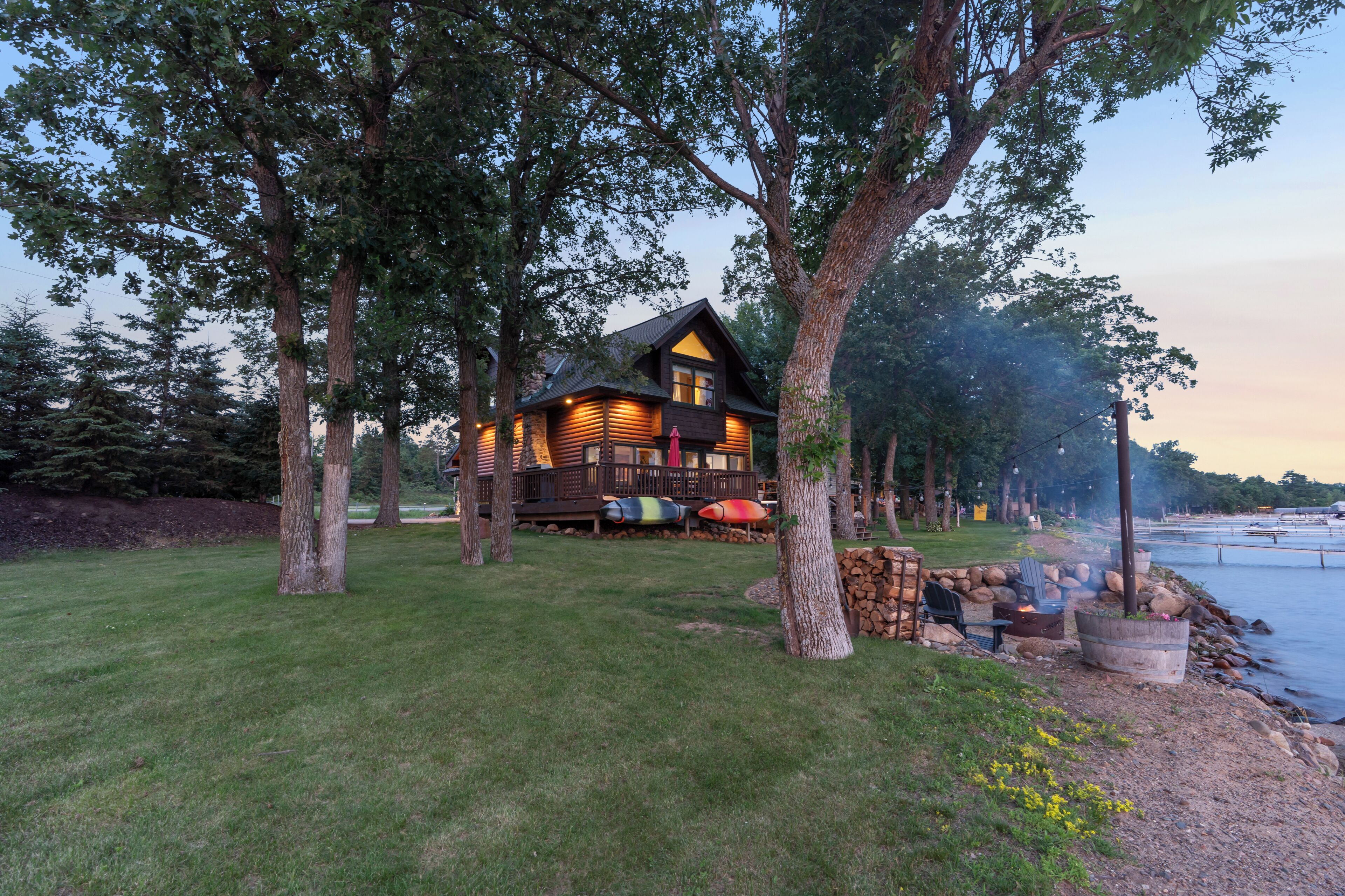 A cabin with a deck, surrounded by trees, near a body of water.
