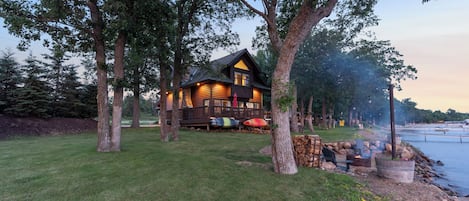 Eine Holzhütte mit einer Terrasse, umgeben von Bäumen, in der Nähe eines Gewässers.