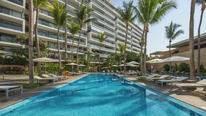 A swimming pool with lounge chairs and umbrellas, surrounded by palm trees and a multi-story building. - Luxury Corner Condo at Nima Bay | Marina Vallarta (Puerto Vallarta)