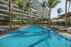 A swimming pool with lounge chairs and umbrellas, surrounded by palm trees and a multi-story building. - Luxury Corner Condo at Nima Bay | Marina Vallarta (Puerto Vallarta)