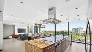A modern kitchen with a large island, built-in oven, and a dining area with a view of the city. - Luxury Corner Condo at Nima Bay | Marina Vallarta (Puerto Vallarta)