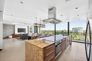 A modern kitchen with a large island, built-in oven, and a dining area with a view of the city. - Luxury Corner Condo at Nima Bay | Marina Vallarta (Puerto Vallarta)