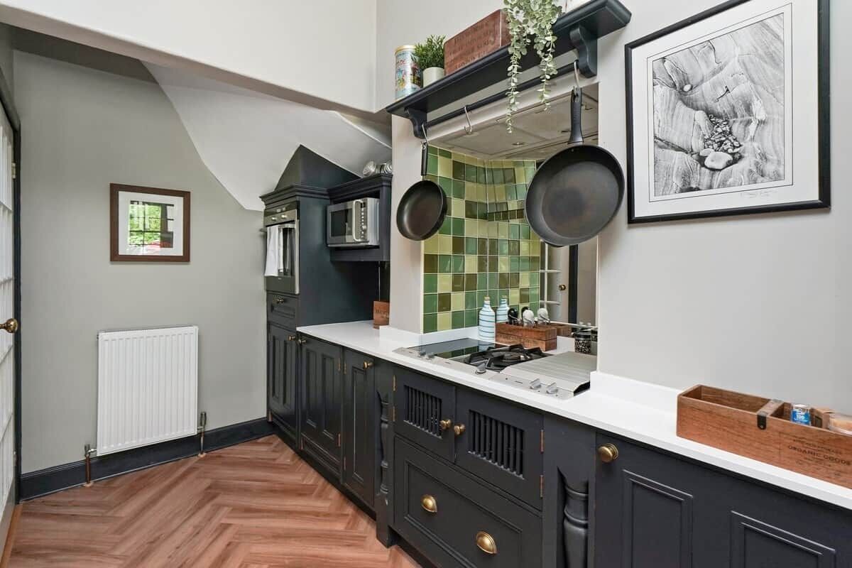 Une cuisine avec des meubles de couleur sombre, un plan de travail blanc et un dosseret de carrelage vert.