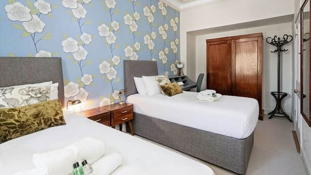 A hotel room with two beds, a wooden wardrobe, a desk, and a large mirror.