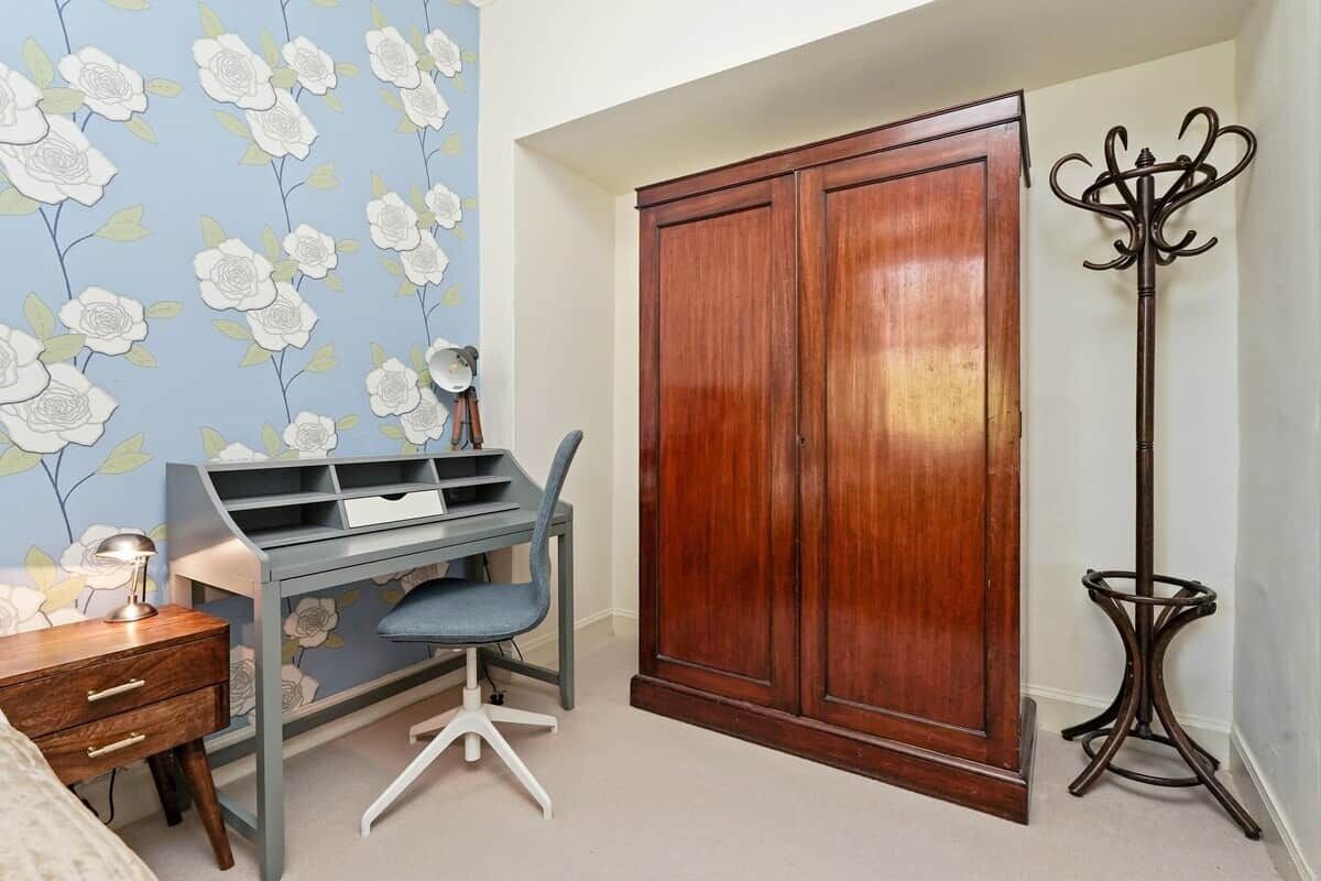 A bedroom with a desk, wardrobe, and a floor lamp.