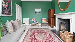 A living room with a green wall, a fireplace, a sofa, two armchairs, and a large rug.