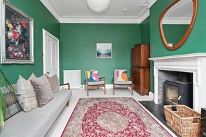 A living room with a green wall, a fireplace, a sofa, two armchairs, and a large rug.