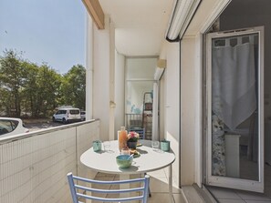 Ein Balkon mit Tisch und Stühlen für zwei Personen und Blick auf die Straße mit parkenden Autos.