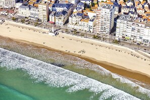 Eine Luftaufnahme einer Küstenstadt mit einem breiten Sandstrand, einer Gebäudepromenade und freiem Blick auf den Ozean.