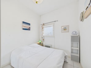 A bedroom with a bed, a nightstand, a window with curtains, a radiator, and a wall-mounted shelf. - Near Port Olona - Apartment for 4 (Les Sables-d´Olonne)