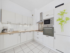 A modern kitchen with white cabinetry, stainless steel appliances, and a digital clock. - Near Port Olona - Apartment for 4 (Les Sables-d´Olonne)