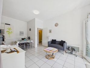 Een moderne woonkamer met een grijze bank, een kleine ronde tafel, en een eethoek met stoelen en een tafel.